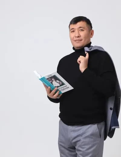 Қалдарбек Сраилов ашық кітап ұстап тұр, иығында пиджак